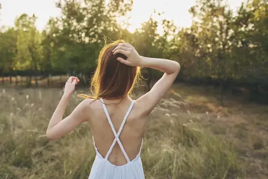 Рыжеволосая девушка в белом платье со спины в поле на закате