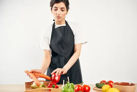 Молодая женщина в фартуке раскладывает свежие овощи на кухне