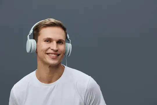 Улыбающийся парень в белых наушниках на сером фоне