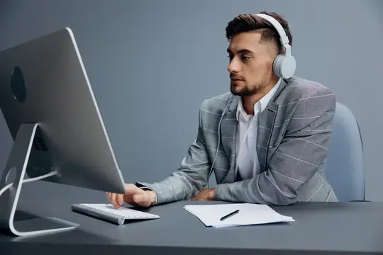 Молодой мужчина в наушниках работает за компьютером в офисе