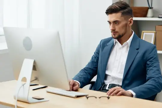 Сосредоточенный мужчина в синем пиджаке работает за компьютером в офисе