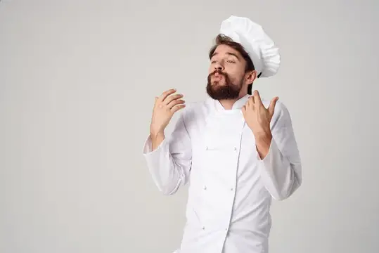 Бородатый повар в белом колпаке жестом показывает вкусно