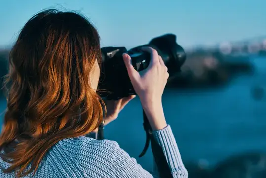 Рыжеволосая девушка фотографирует пейзаж на камеру