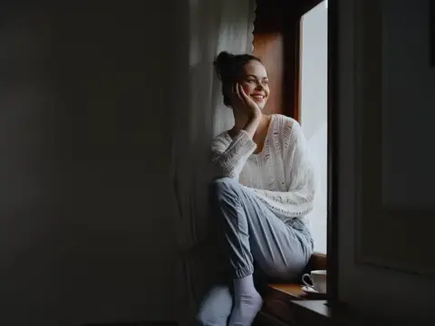 Красивая женщина сидит у окна деревянного дома с телефоном в руке