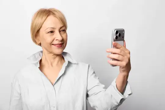 Улыбающаяся блондинка в белой рубашке делает селфи на смартфон
