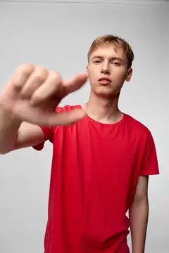 Крупный студийный кадр молодого человека в красной футболке, протягивающего руку к объективу, подчёркивающий глубину, фокус и вовлечённость через смелый жест и современную композицию