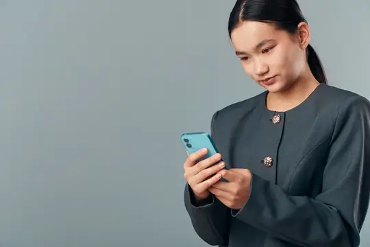 Азиатская девушка в сером жакете смотрит в смартфон