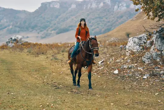 Рыжеволосая девушка верхом на гнедом коне среди осенних гор