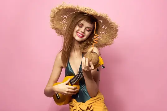 Улыбающаяся девушка в соломенной шляпе с кокосом и укулеле на розовом фоне
