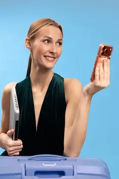 Улыбающаяся светловолосая женщина с ноутбуком и смартфоном у чемодана