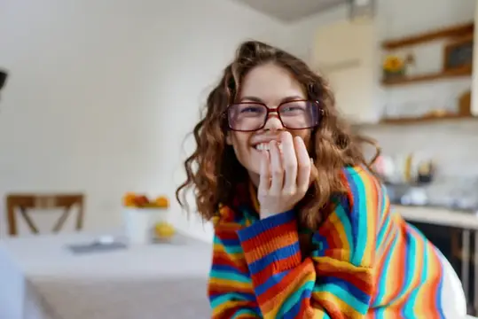 Кудрявая девушка в очках смеётся на кухне