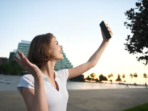 Молодая женщина делает селфи на смартфон на закате у воды
