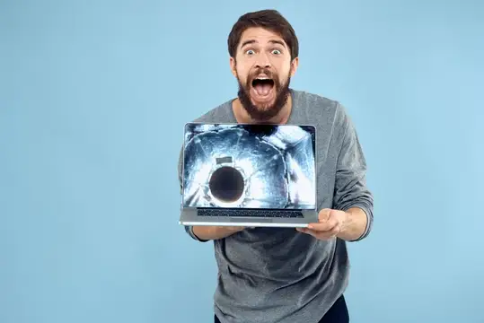 Бородатый мужчина с ноутбуком с удивлением смотрит на экран