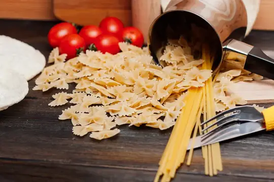 Макароны бантики и спагетти рассыпаны на тёмном столе рядом с помидорами