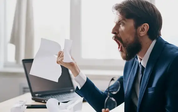 Разъяренный бородатый мужчина в костюме рвет бумагу в офисе