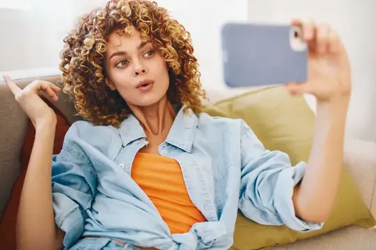 Кудрявая девушка делает селфи на смартфон, лежа на диване
