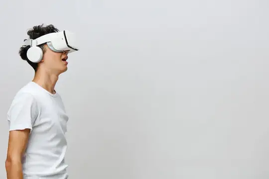 Молодой человек в белой футболке и VR-очках на сером фоне