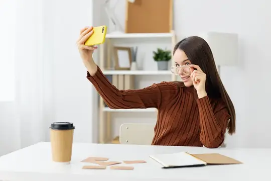 Улыбающаяся девушка-подросток сидит за столом с книгой и телефоном