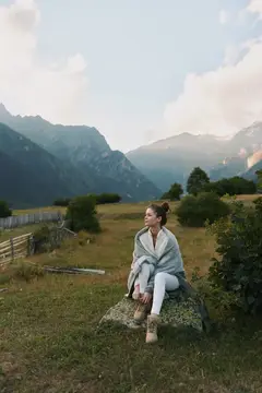 Молодая женщина в пледe сидит на камне в горах