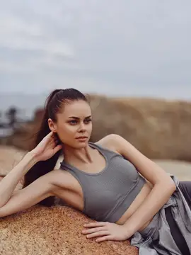 Спортивная брюнетка в сером топе отдыхает на камне