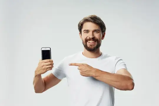 Бородатый мужчина в белой футболке показывает на смартфон