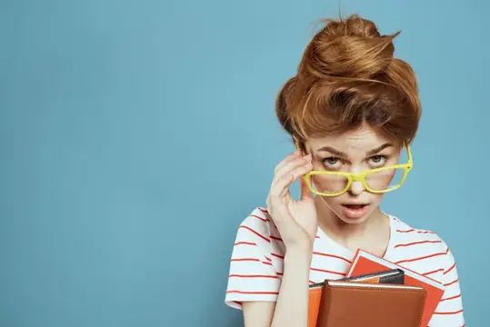 Рыжеволосая девушка в жёлтых очках с книгами удивлённо смотрит на синем фоне