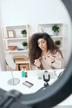 Кудрявая девушка записывает видео о макияже на смартфон