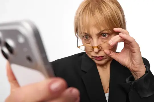 Пожилая женщина в очках внимательно смотрит в смартфон