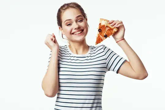 Улыбающаяся девушка в полосатой футболке держит кусок пиццы