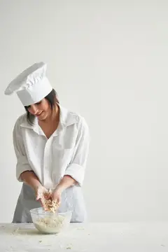 Улыбающаяся повариха в колпаке готовит тесто на светлой кухне