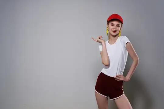 Улыбающаяся девушка в красной кепке и белой футболке жестом показывает в сторону