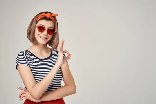 Улыбающаяся девушка в красных очках показывает жест ОК