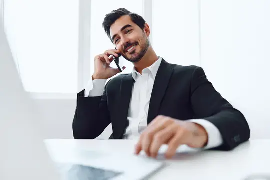 Улыбающийся бородатый мужчина в костюме говорит по телефону в офисе