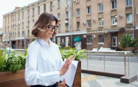 Женщина на улице возле цветов показывает документы в папке