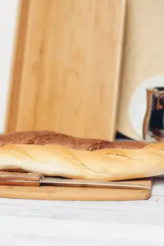 Длинный багет лежит на деревянной доске на кухне