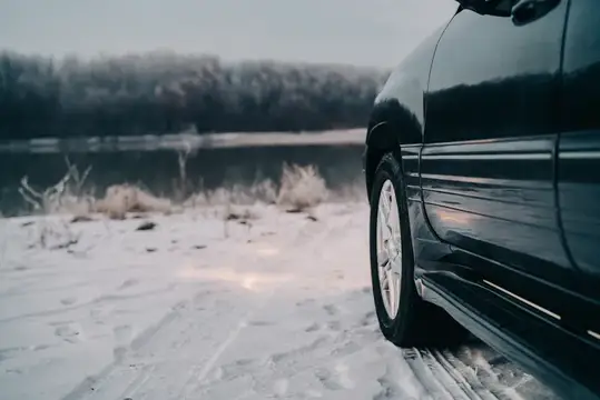 Черный автомобиль на заснеженном берегу озера зимой
