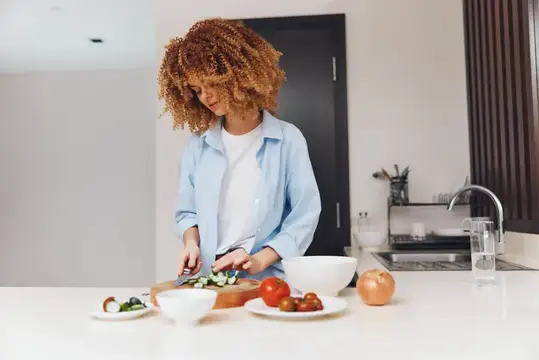 Кудрявая женщина режет овощи на кухне