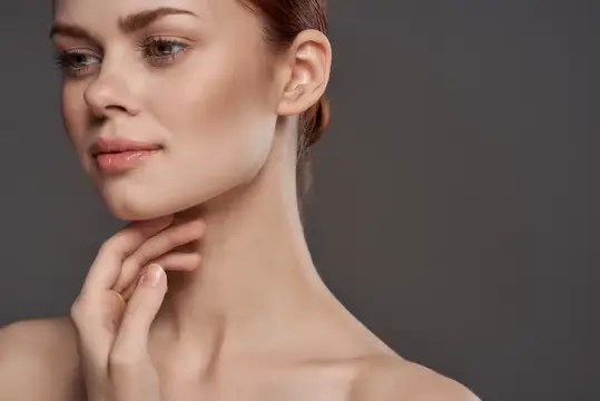 Молодая женщина с естественным макияжем касается шеи на сером фоне