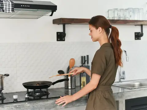 Рыжеволосая девушка готовит на плите на светлой кухне