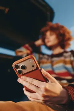 Руки держат смартфон в рыжем чехле на фоне размытой девушки