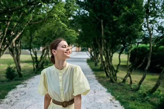 Молодая женщина в бледно-жёлтом платье на аллее парка