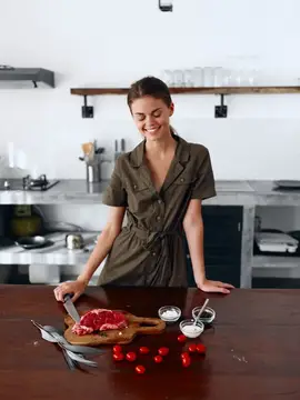 Улыбающаяся молодая женщина режет мясо на кухне