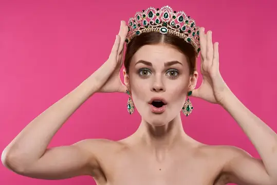 Удивленная девушка в роскошной короне на розовом фоне
