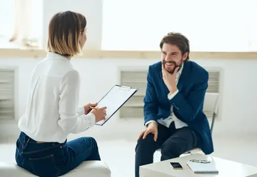 Улыбающийся мужчина в синем пиджаке беседует с женщиной с планшетом