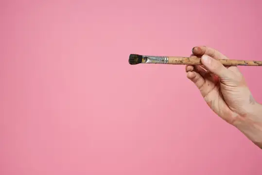 Рука держит кисть для рисования на розовом фоне