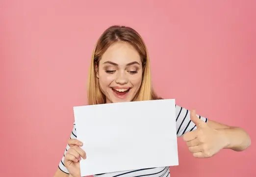 Светловолосая девушка с белым листом и жестом одобрения на розовом фоне