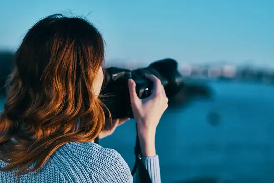 Рыжеволосая девушка фотографирует на камеру у моря