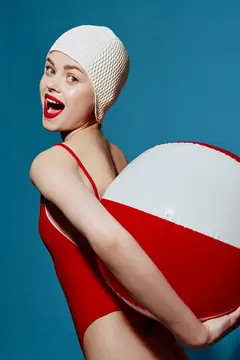 Улыбающаяся девушка в красном купальнике и белой шапочке с пляжным мячом