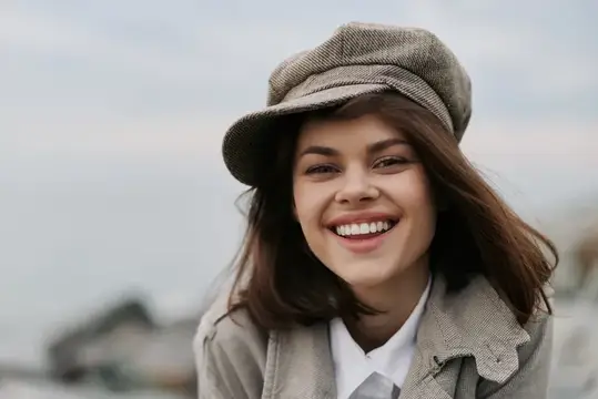 Улыбающаяся девушка в кепке и пальто на улице