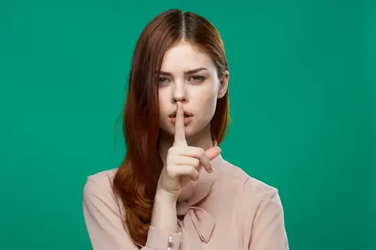 Рыжеволосая девушка прикладывает палец к губам на зелёном фоне